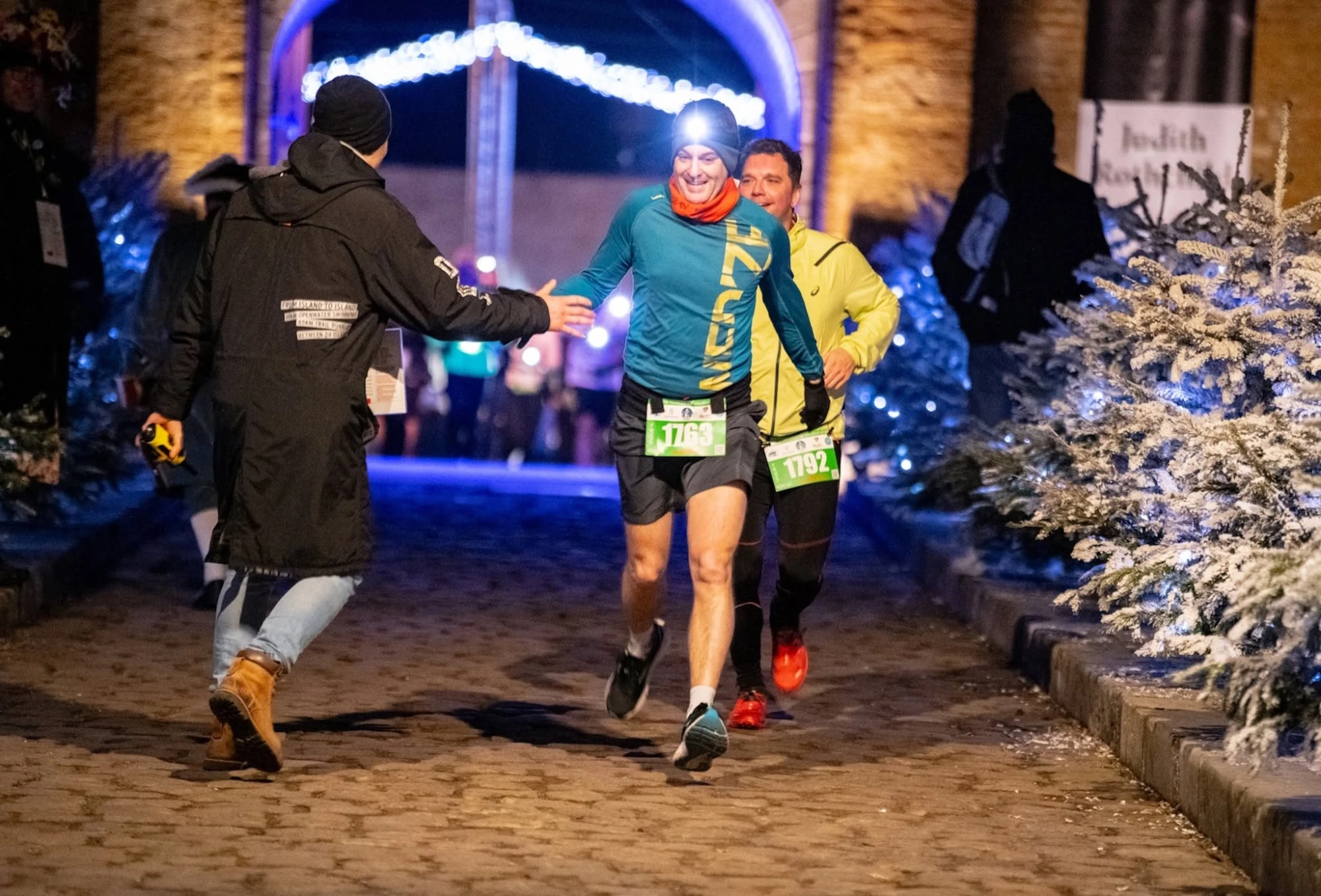 Un coureur salue un bénévole sous l'arche d'arrivée illuminée